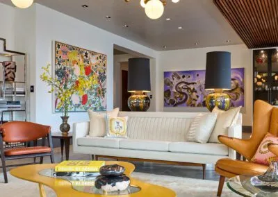 A stylish living room featuring a sleek sofa, a vibrant chandelier, and captivating artwork. The space is elegantly designed with mid-century modern furniture, including a distinctive coffee table and armchairs. The room offers a perfect blend of comfort and contemporary aesthetics. Get in Touch for more information on creating your dream home.